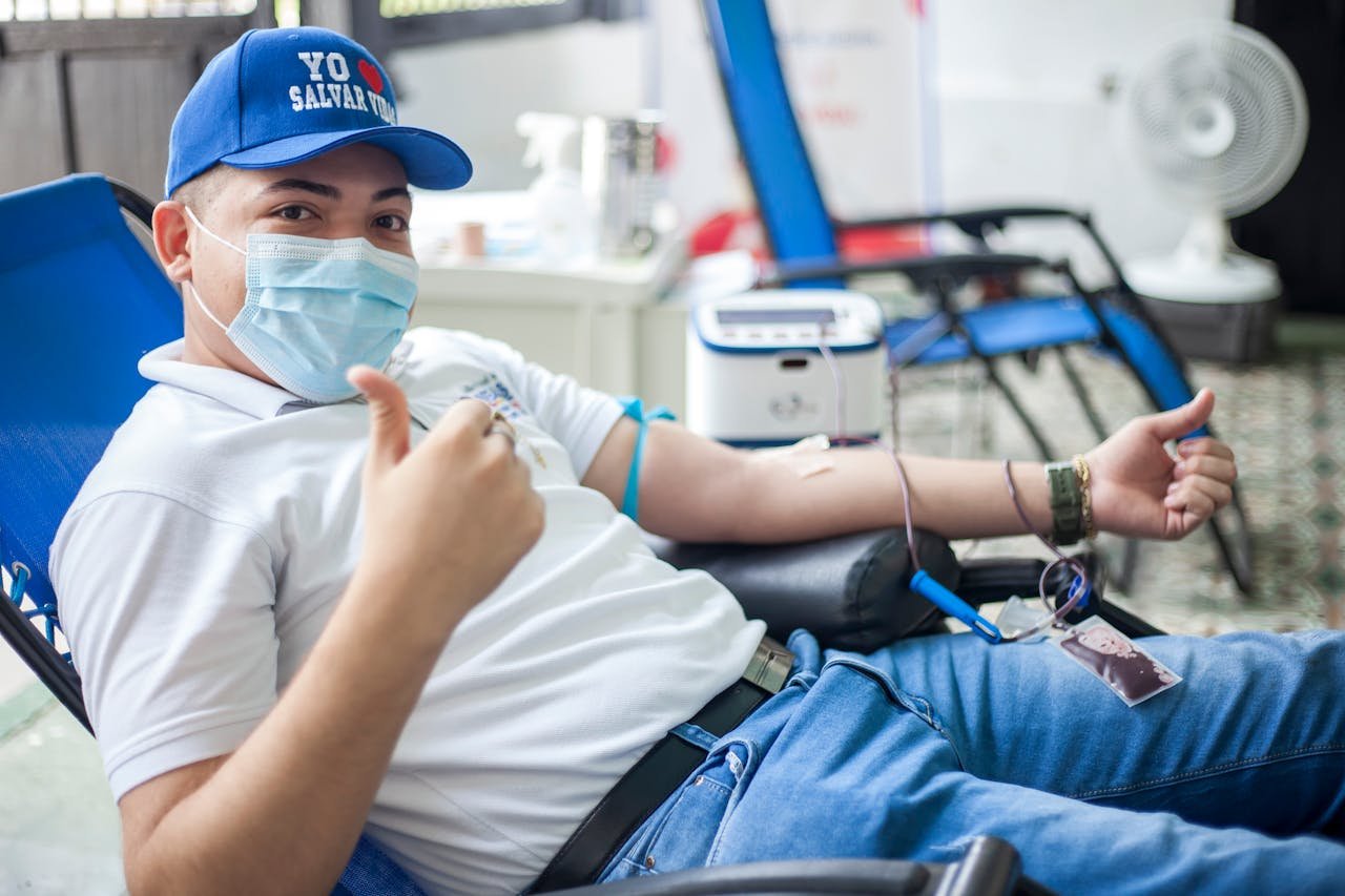 Man donating blood while giving a thumbs up, promoting blood donation in a friendly setting.